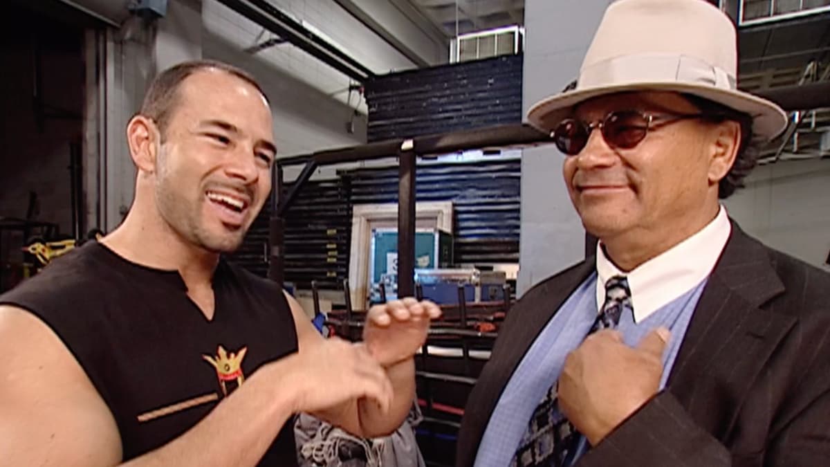 Chavo Classic with a fedora and sunglasses looking at a happy Chavo Guerrero