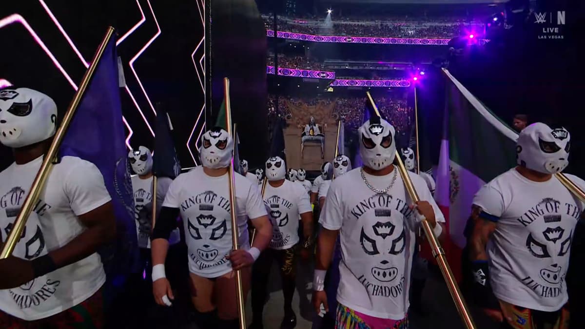 Dominik Mysterio sitting on a giant throne as a whole host of luchadores stand in front of him 