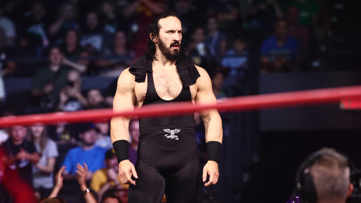 PAC walks towards a wrestling ring, with a towel draped over the back of his neck and shoulders