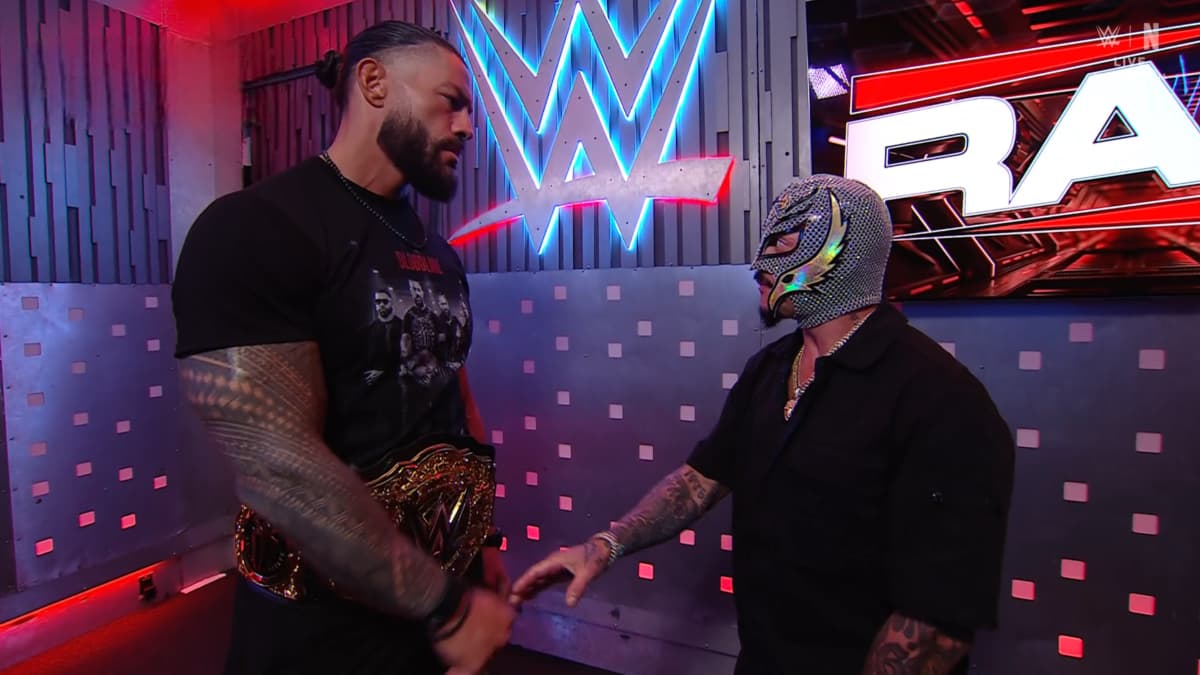 Roman Reigns looking down at Rey Mysterio as he offers to shake his hand