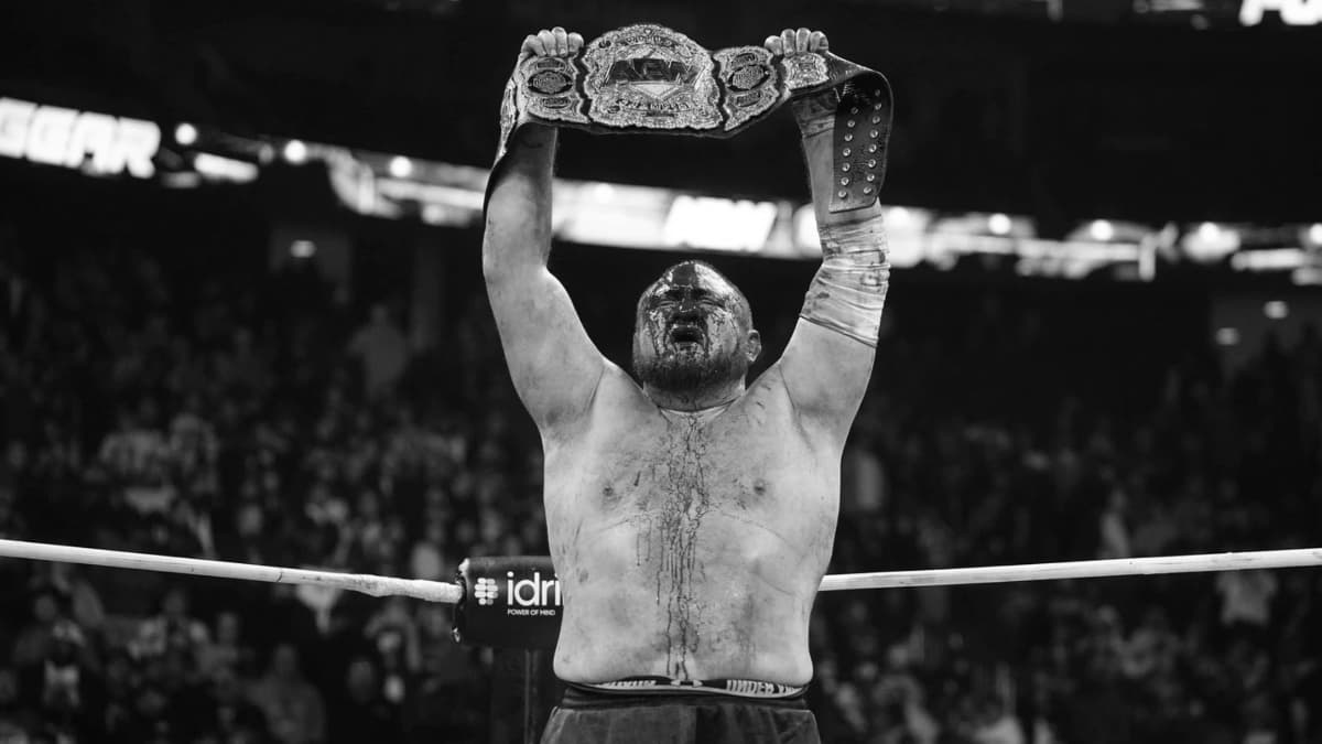 Samoa Joe holding up the AEW World Title while covered in blood