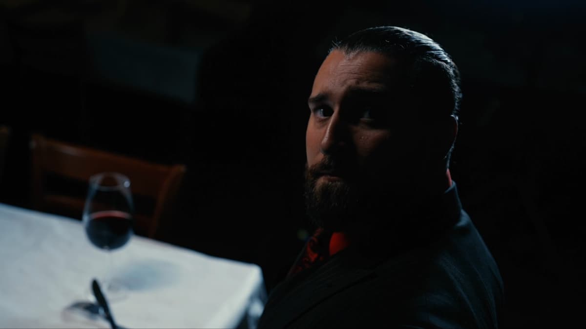 Tony D'Angelo in a suit looking up in the camera as darkness begins to shroud him