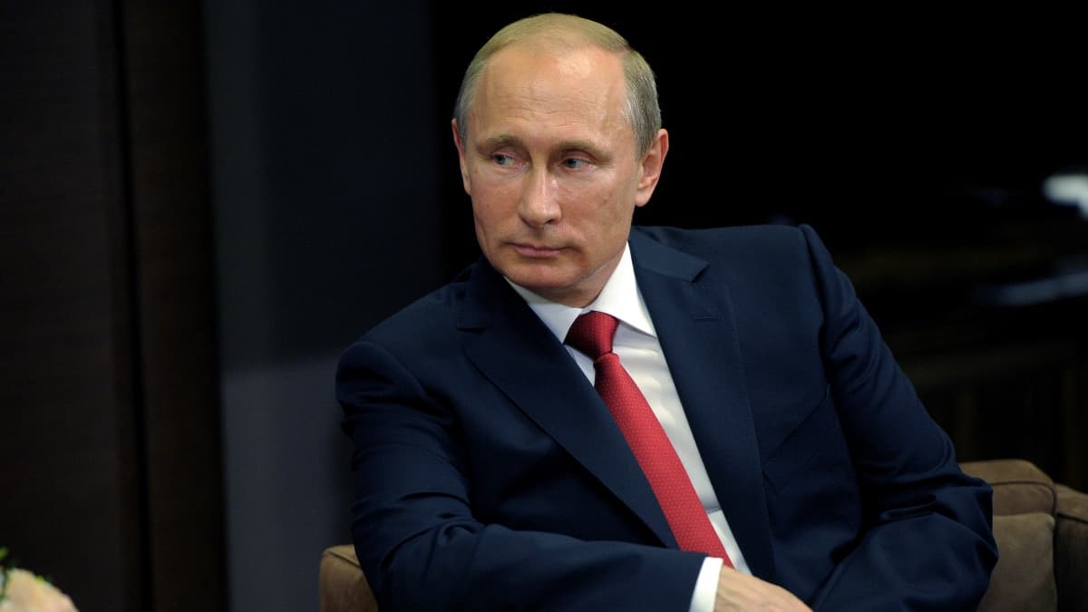 Vladimir Putin sitting down wearing a blue suit and red tie