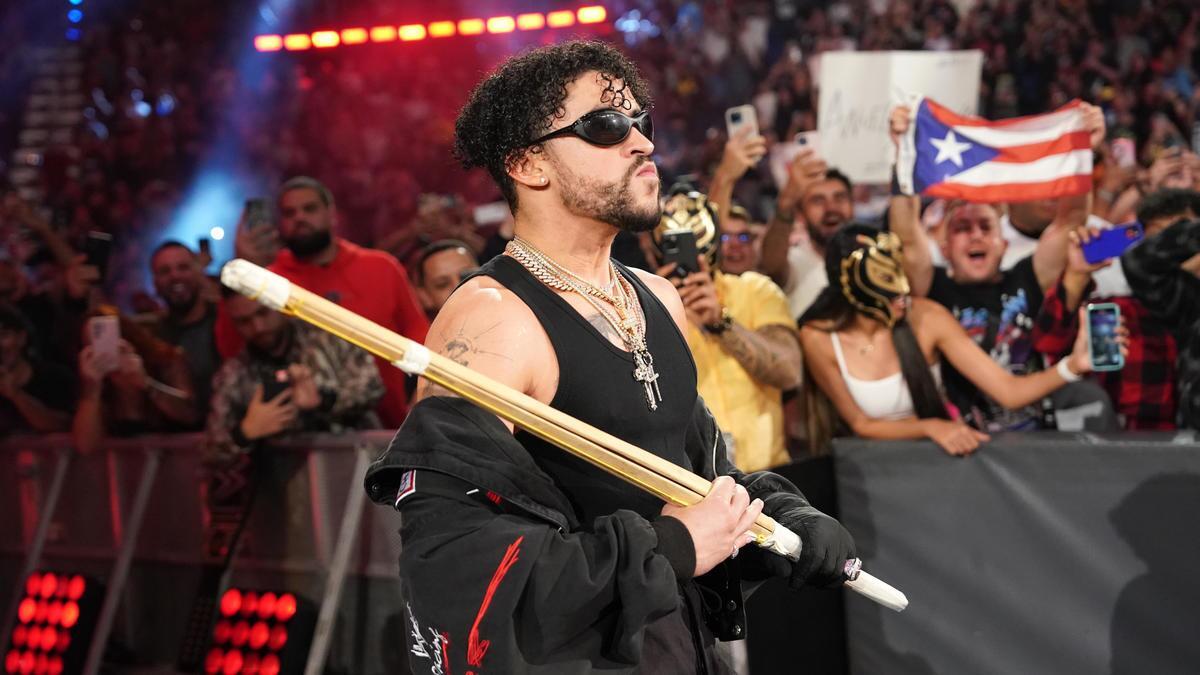 Bad Bunny in sunglasses holding a kendo stick and staring off camera at a WWE event