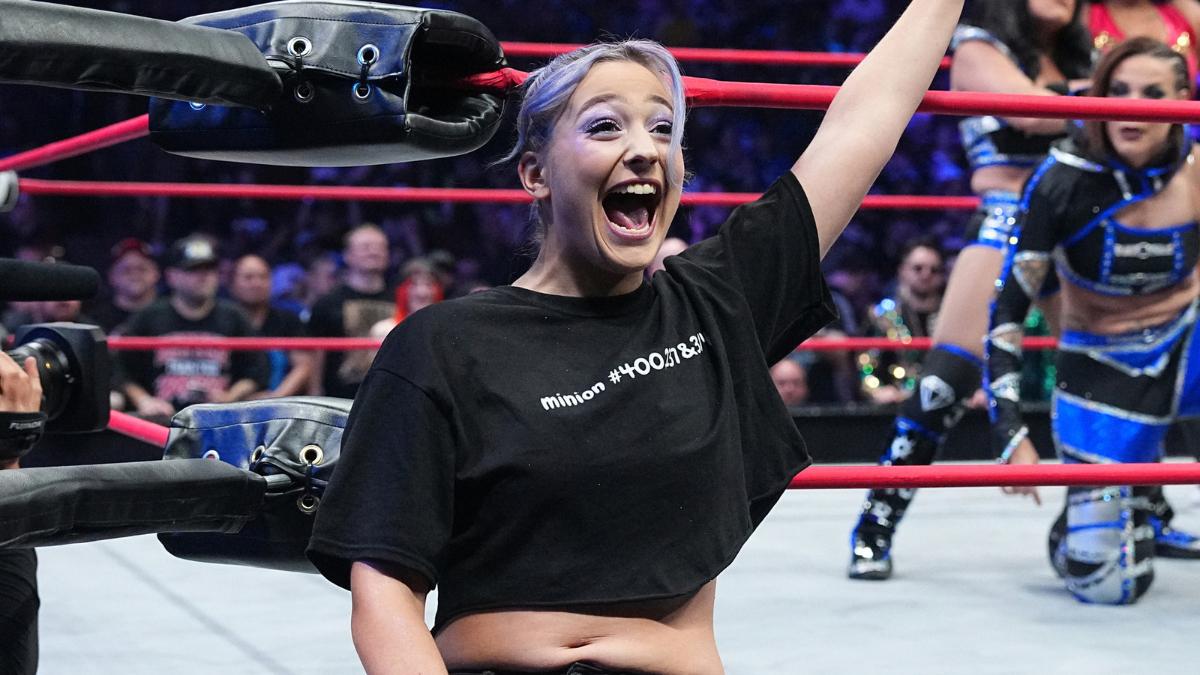 Billie Starkz outside a wrestling ring happily yelling and waving at the audience