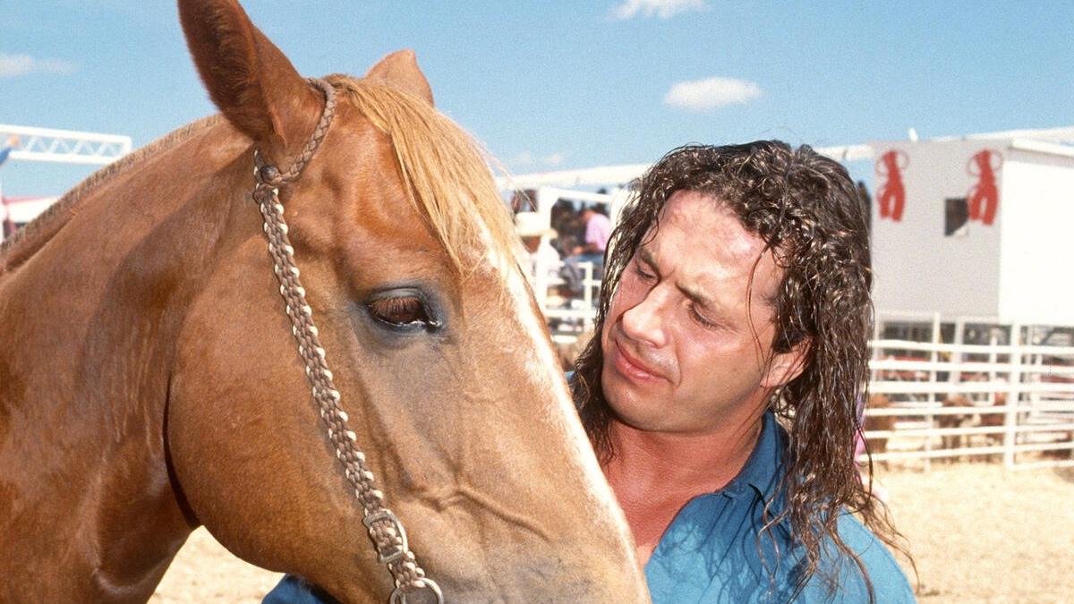Bret Hart in a denim shirt looking at a brown horse