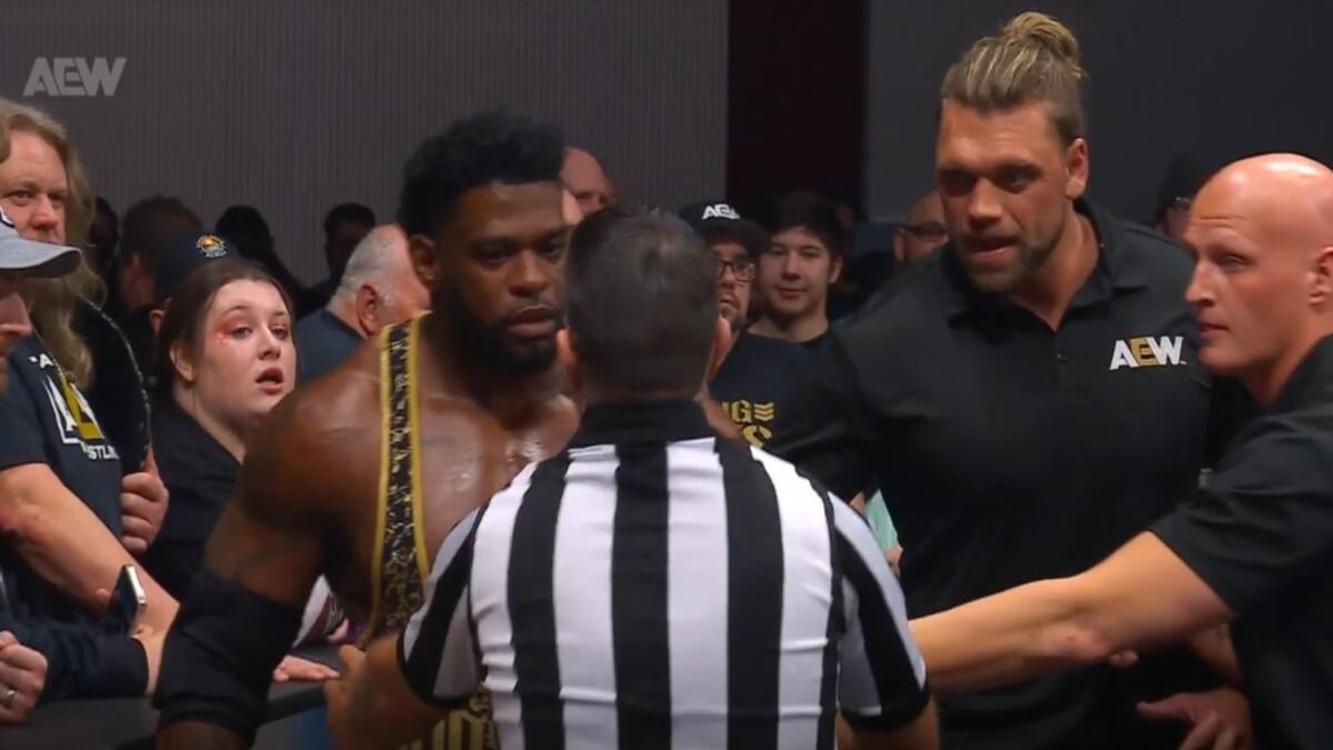 Powerhouse Hobbs in front of fans talks with a referee as Cal Bloom acts as security on the right