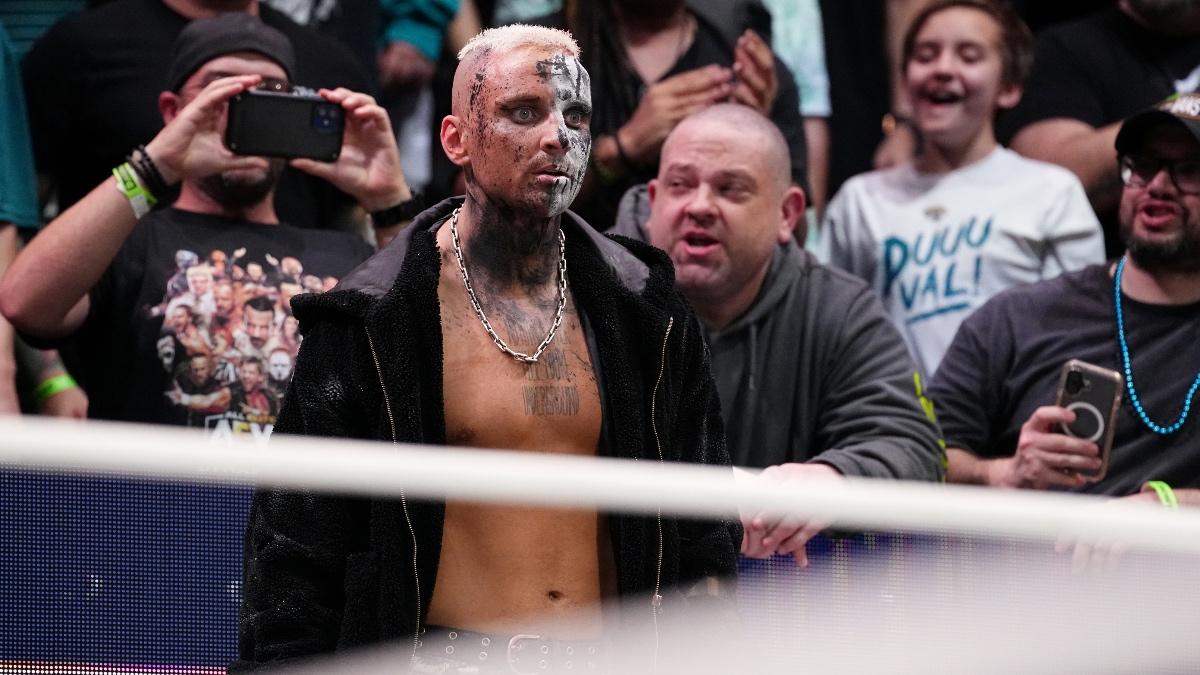 Darby Allin with missing face paint staring at the ring with a bald fan behind him