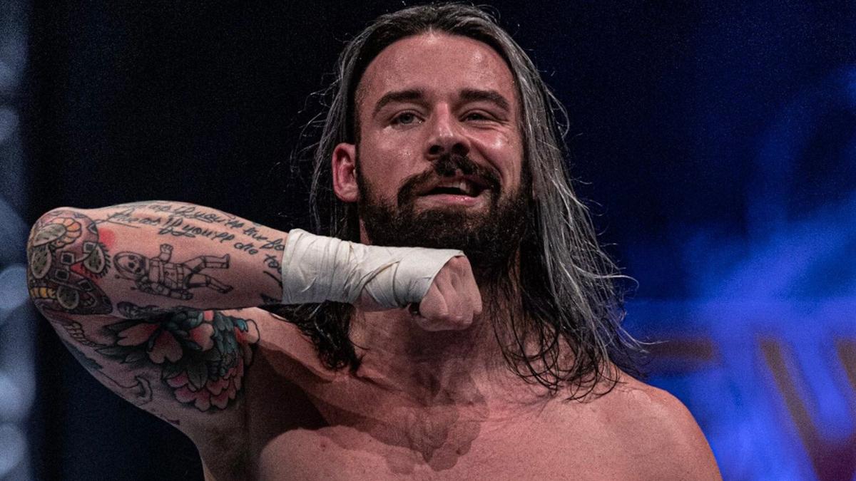 David Finlay smirking in a wrestling ring, posing with his forearm and fist under his jaw.