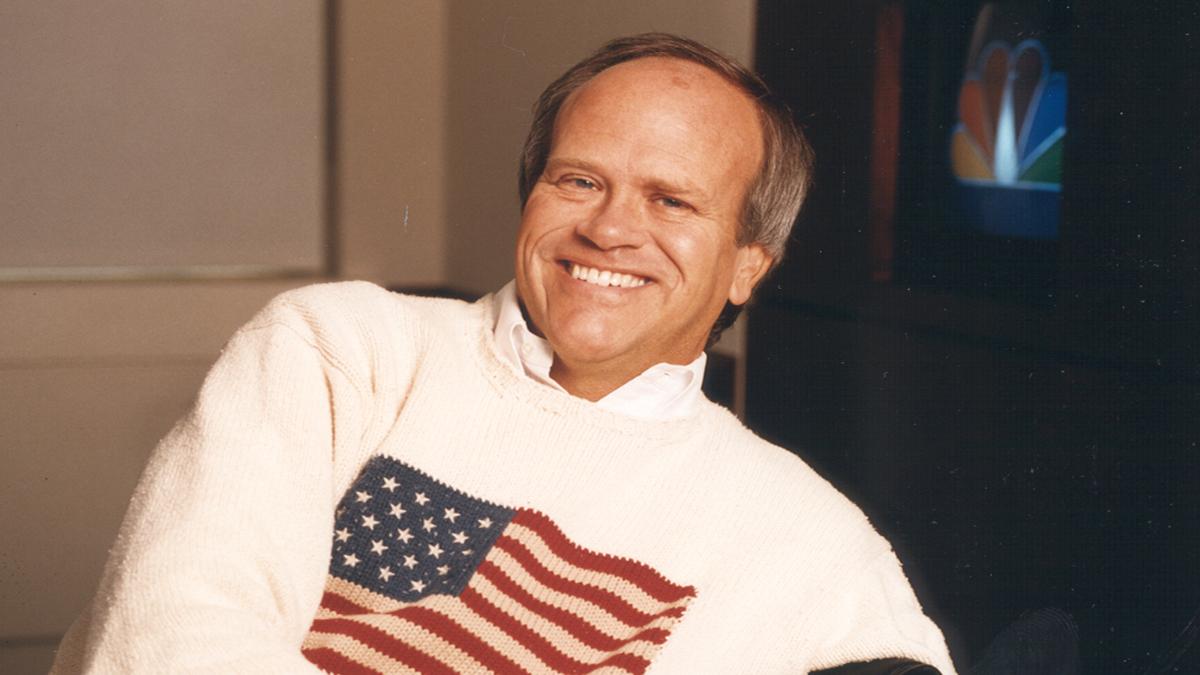 Dick Ebersol in a US flag jumper lounging in a chair and smiling