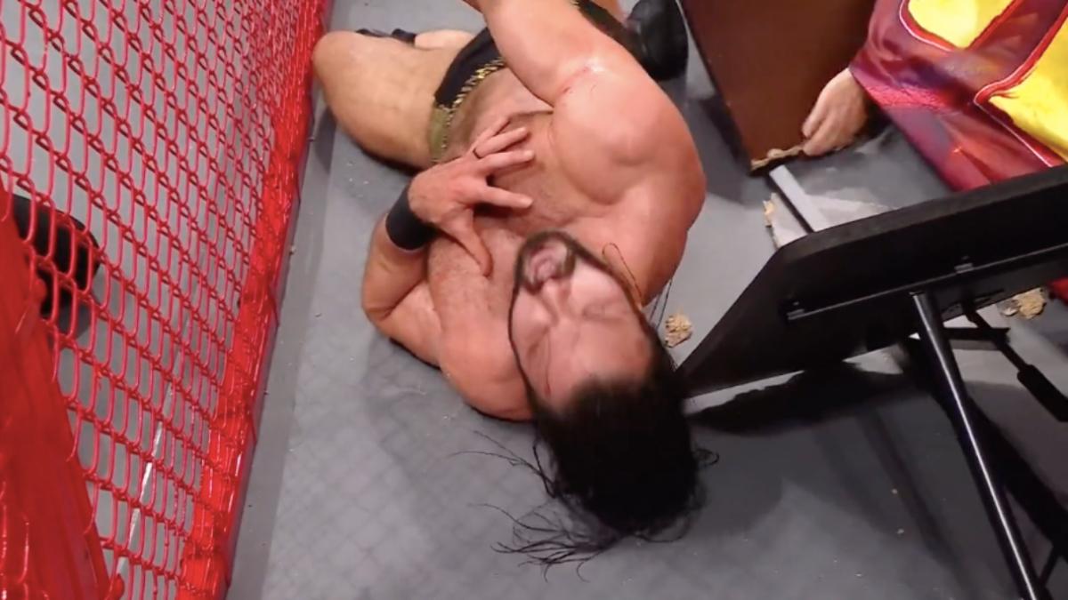 Production member's hand under the ring as Drew McIntyre writhes in pain on the floor at WWE Hell in a Cell 2021