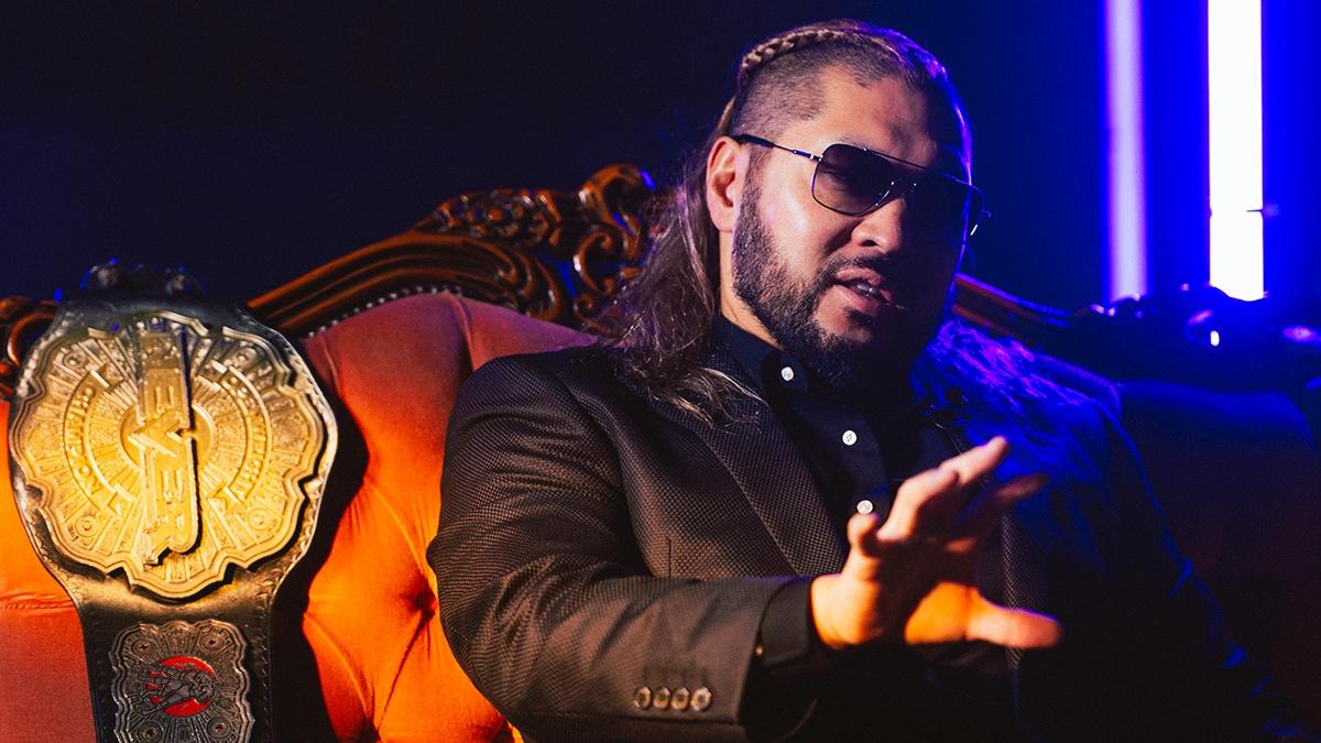 EVIL sitting on a sofa wearing sunglasses and a black suit