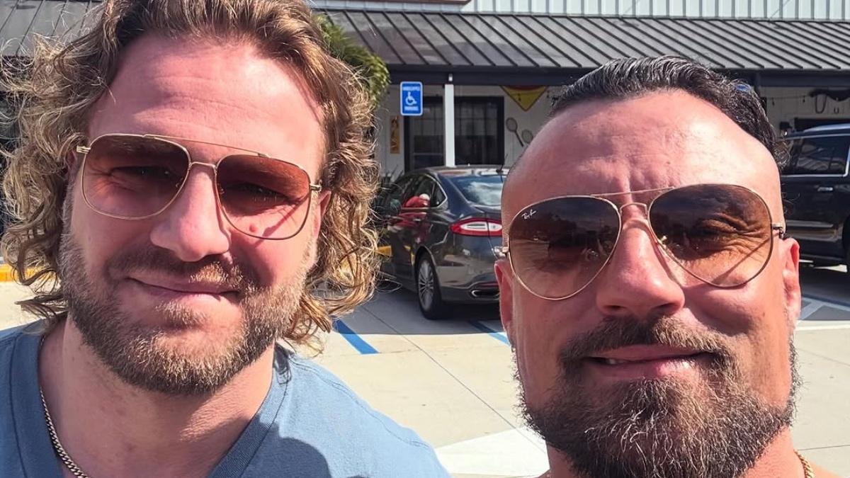 Hangman Page and Marty Scurll wearing sunglasses smiling outside of a Cracker Barrel