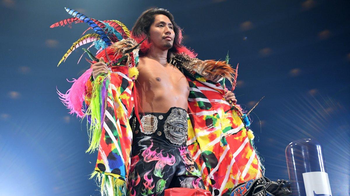 Hiromu Takahashi taking off a multi-coloured feather strewn coat to reveal a wrestling championship around his waist