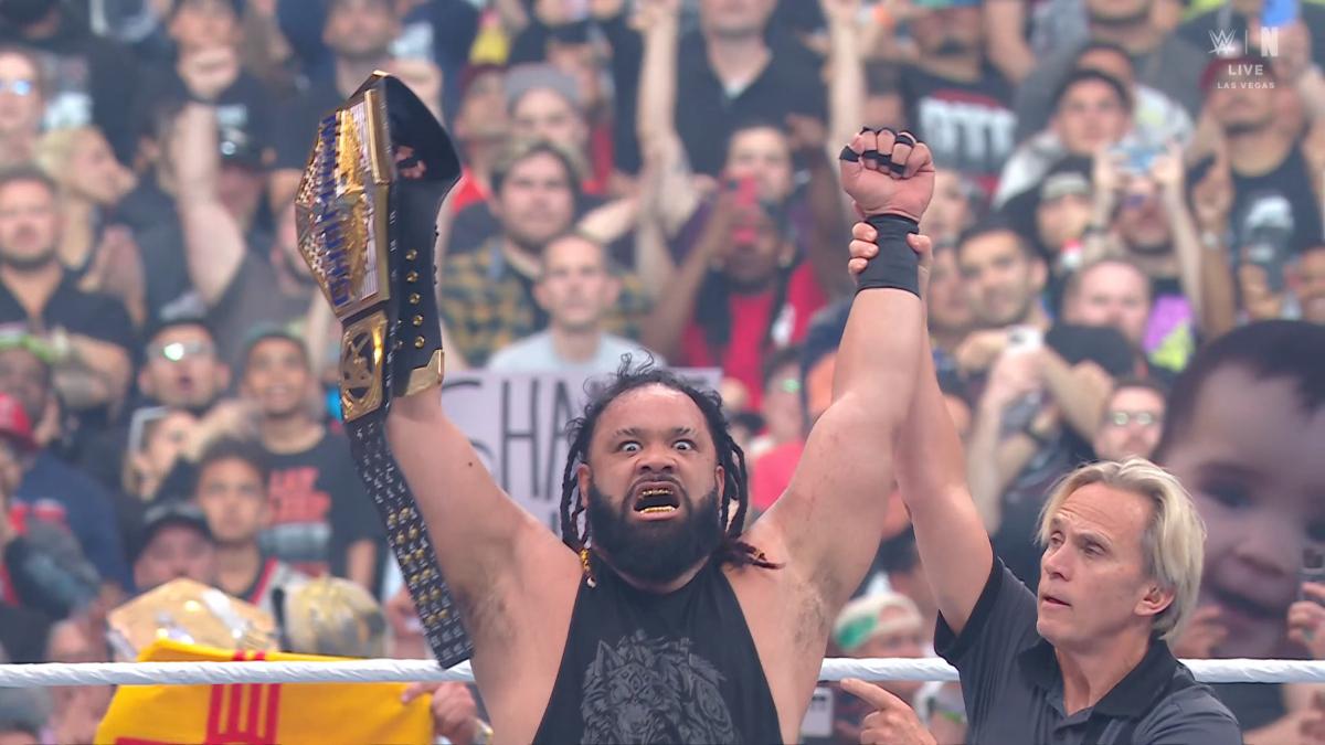 Jacob Fatu holds the US Championship in the air in a WWE ring, the referee raising his arms in victory
