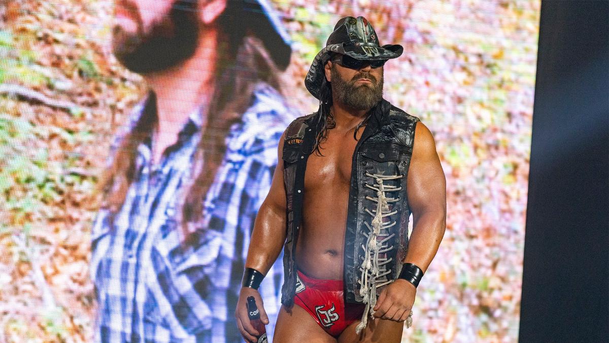 James Storm in hat, sunglasses, and leather vest carrying a beer on his way to a wrestling ring