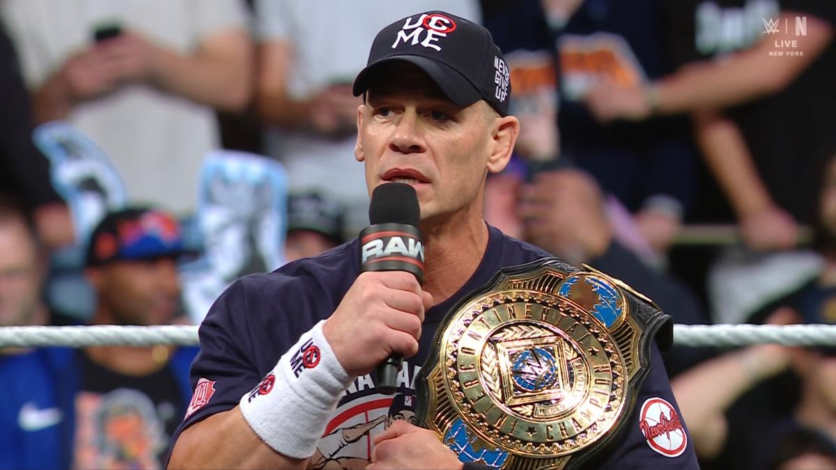 John Cena wearing blue attire cutting a promo with the WWE Intercontinental Title over his left shoulder
