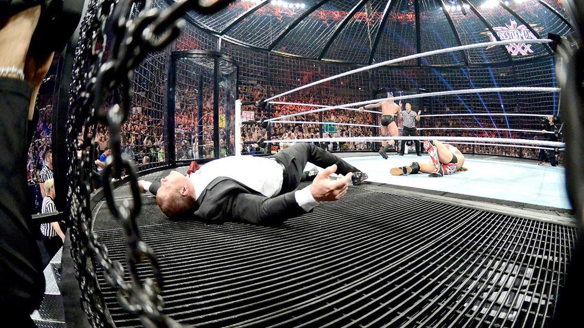 Kane lying down on the steel floor as Randy Orton complains to the referee in the background