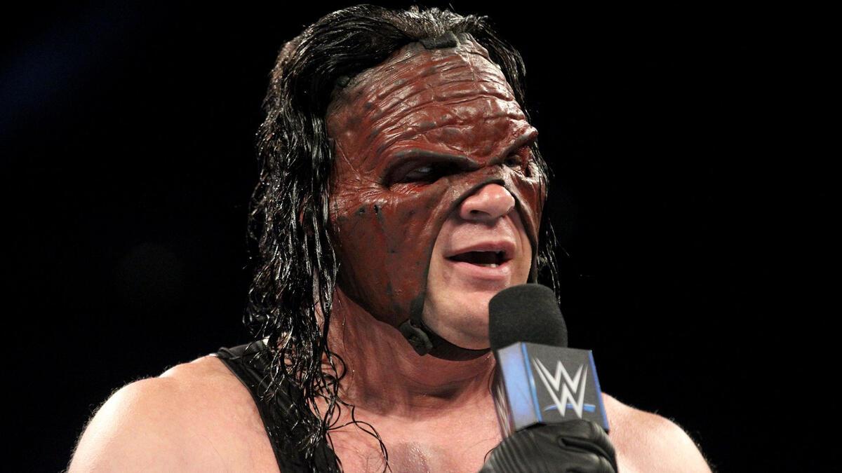 WWE star Kane, wearing a mask, holds the microphone while delivering a promo on SmackDown in 2018