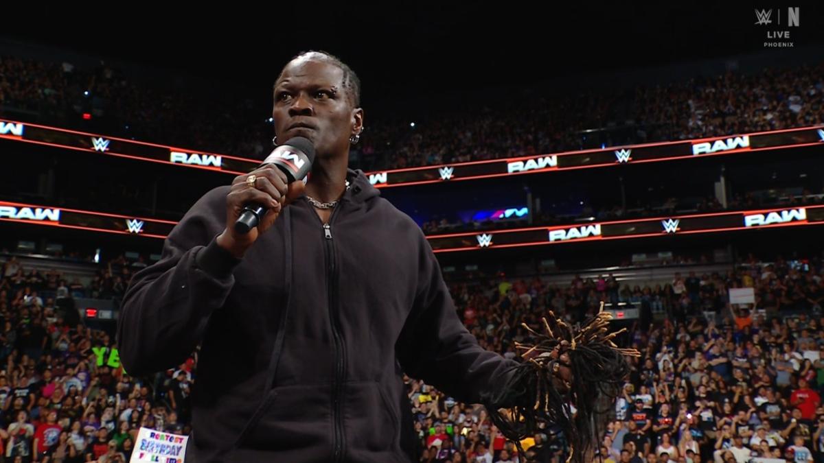 WWE star Ron Killings holds his hair in his left hand and a microphone in his right after cutting his hair off with scissors on WWE Raw