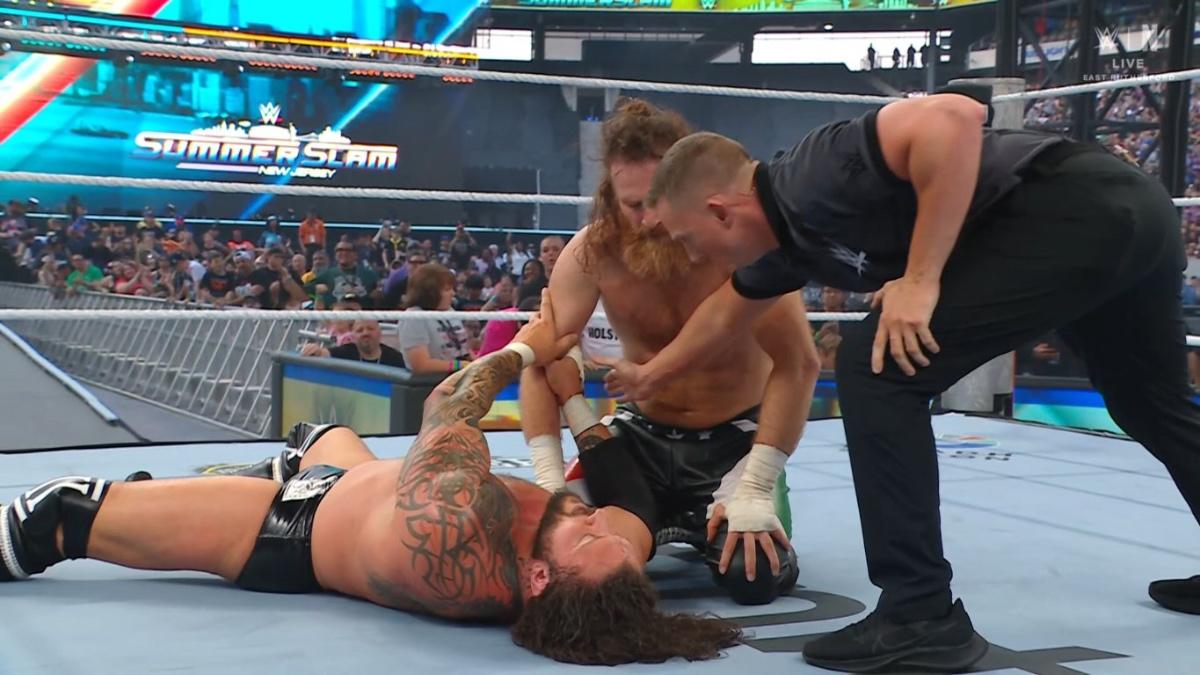 Sami Zayn kneeling down beside Karrion Kross as the referee checks on them at WWE SummerSlam