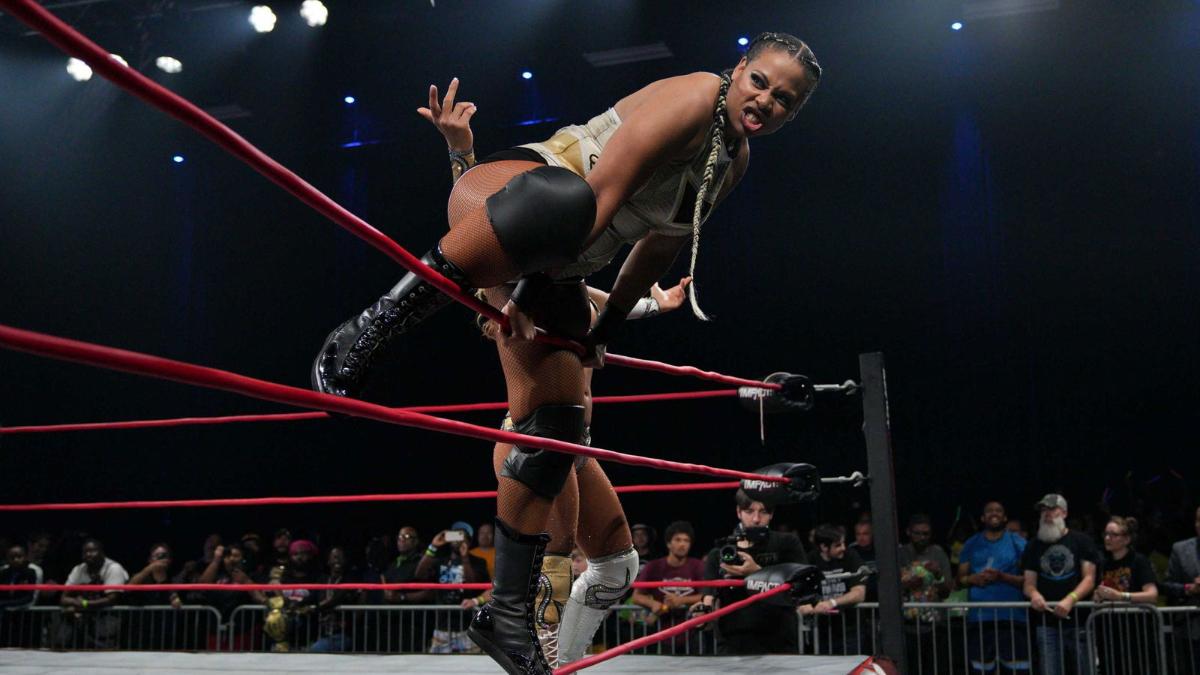 Savannah Evans poses on the ropes of a wrestling ring, with an obscured Gisele Shaw in the background.