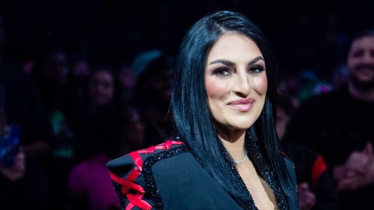 Sonya Deville smiling while wearing a black and red suit