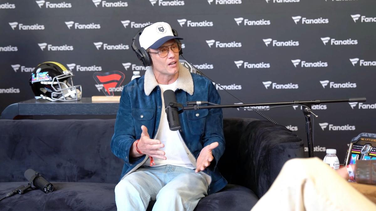 Tom Brady wearing a denim sherpa jacket with yellow-tinted glasses and a cap