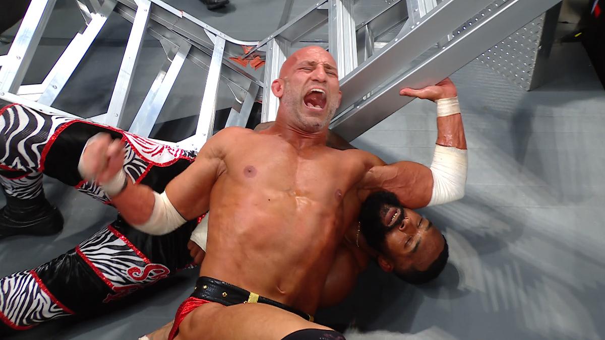 Tommaso Ciampa screaming in pain with Montez Ford asleep underneath him while lying on a ladder