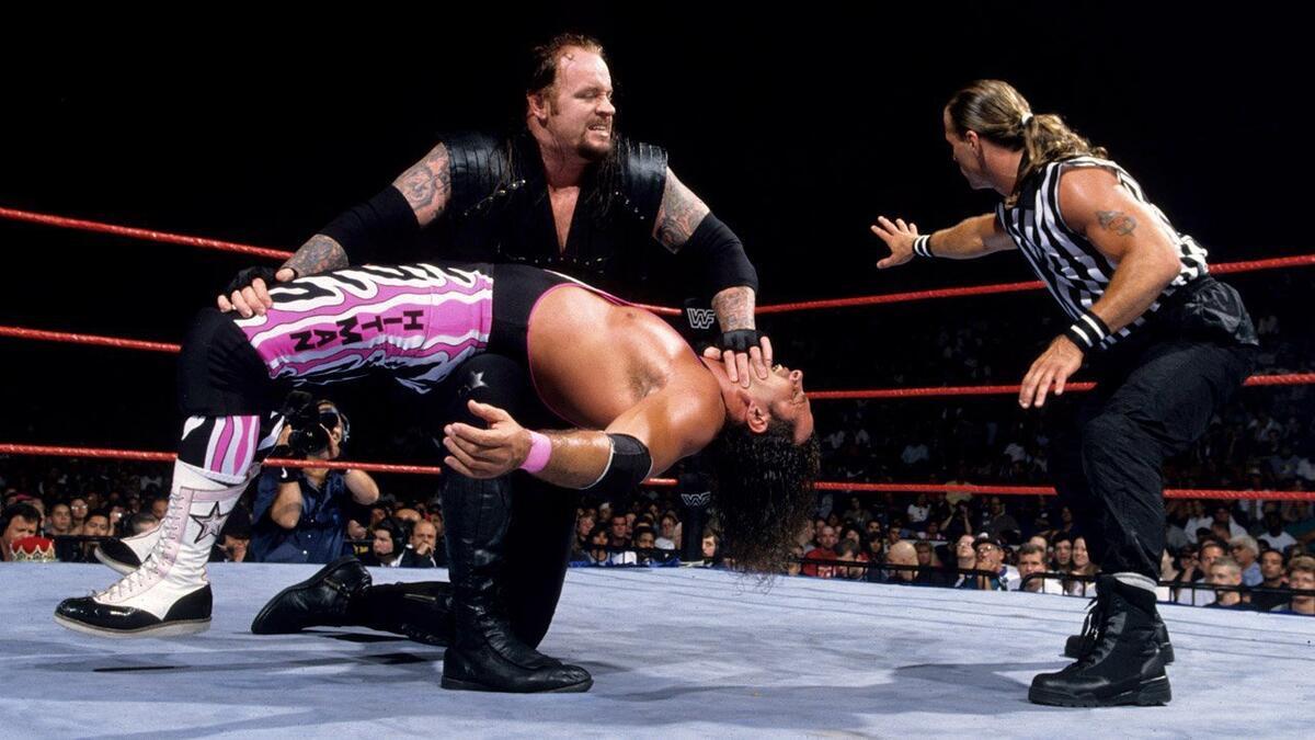 Undertaker stretching Bret Hart as Shawn Michaels looks on at WWE SummerSlam 1997