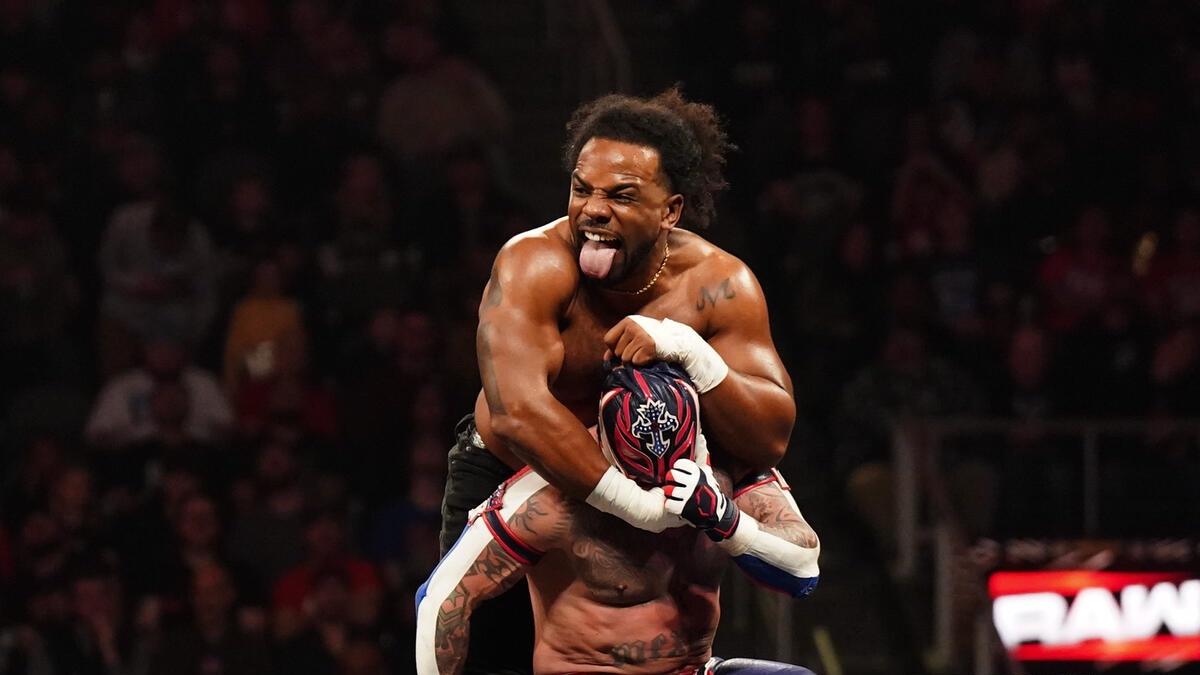 Xavier Woods sticking his tongue out while pulling at Rey Mysterio's mask