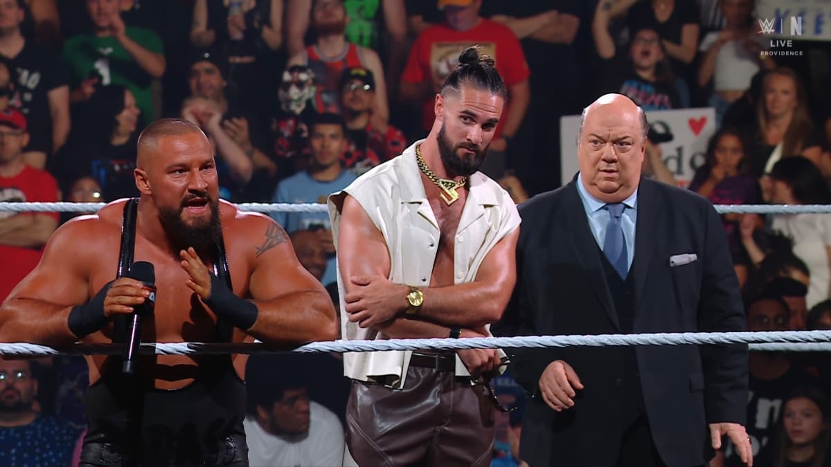 Bron Breakker on the ring ropes while Seth Rollins and Paul Heyman stand behind him