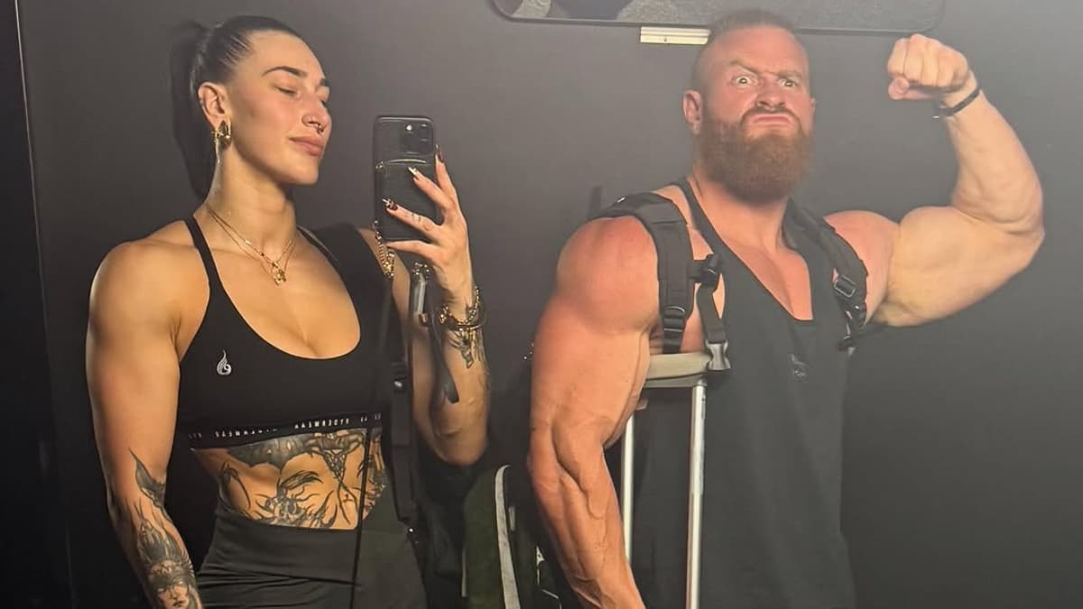 Rhea Ripley taking a selfie with Buddy Matthews while he holds a crutch and flexes