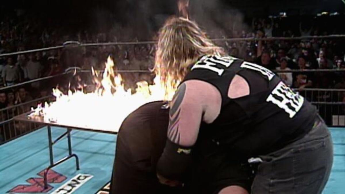 Balls Mahoney about to hit a Powerbomb through a flaming table