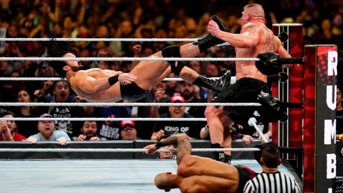 Brock Lesnar leaning on the ring ropes as Drew McIntyre is mid-air about to hit a Claymore kick