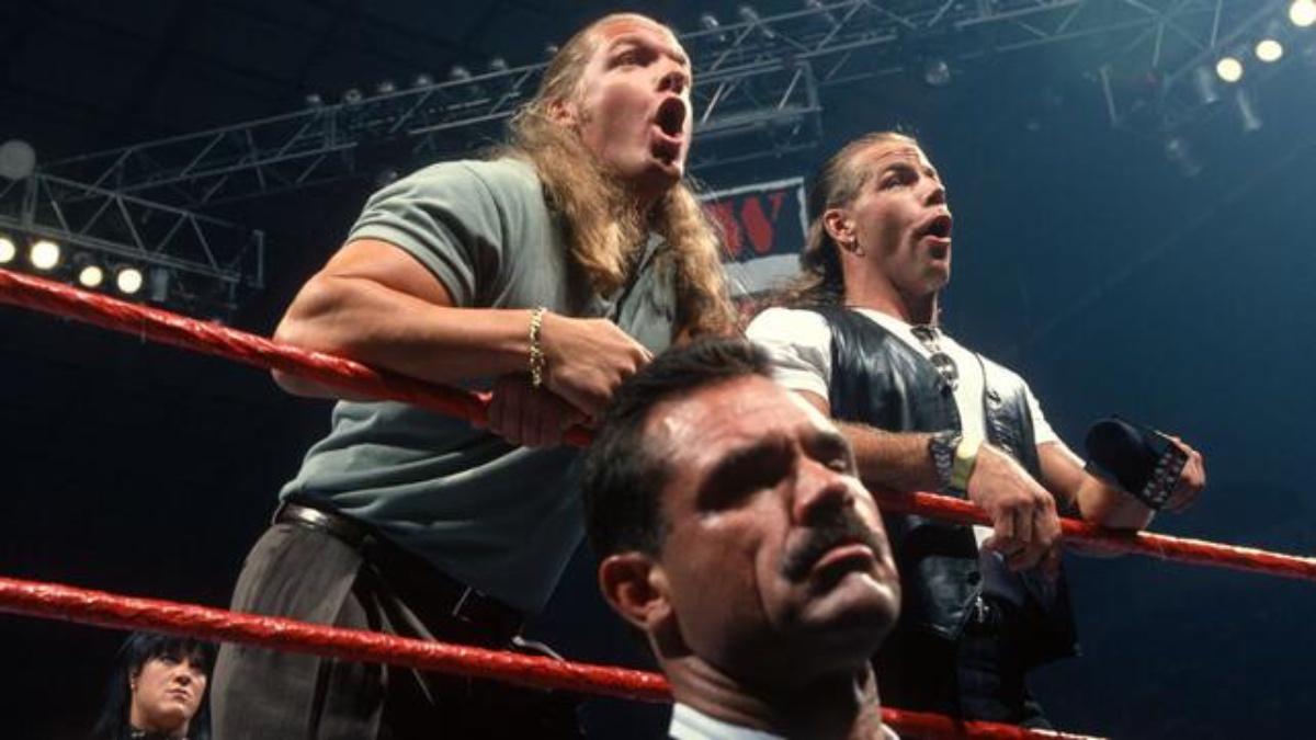 Triple H and Shawn Michaels pulling shocked faces in the ring as Rick Rude stands on the outside